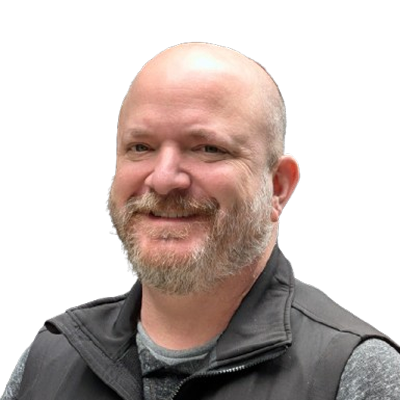 Smiling bald man with a beard wearing a dark gray jacket and shirt against black background.