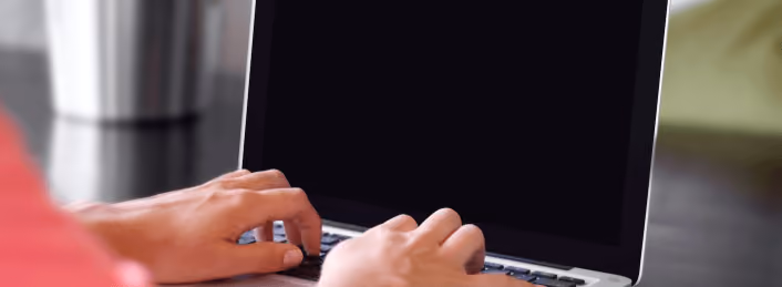 Close-up of hands typing on a laptop keyboard with a blank screen in the background.