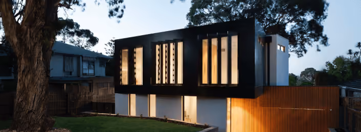 Modern two-story house at dusk with large vertical windows and dark upper facade.