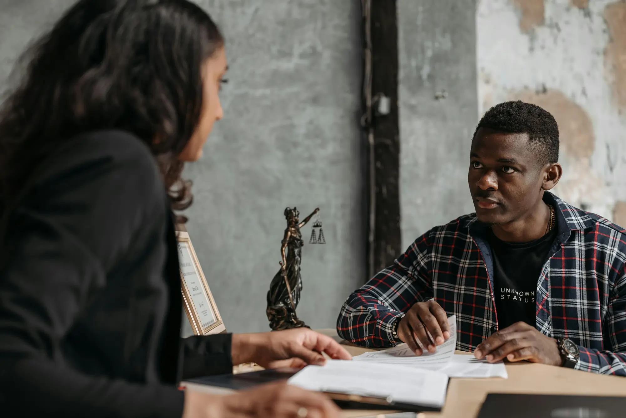 Man and woman discussing documents at a desk with a Lady Justice statue in the background.