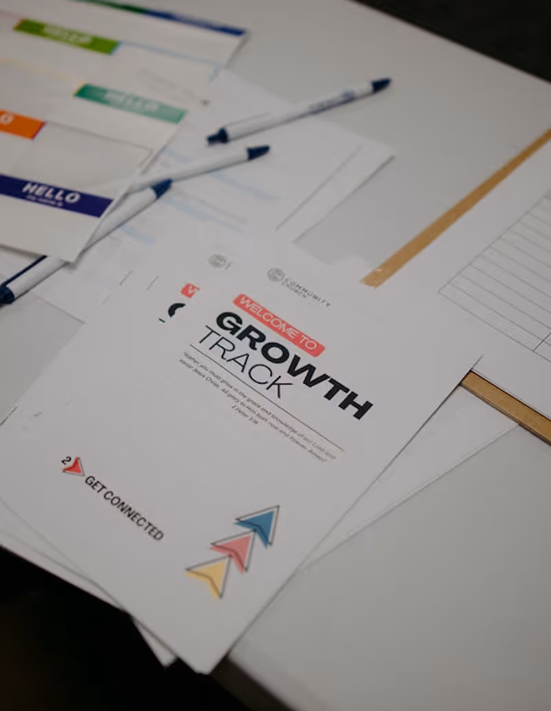 Stack of papers on a table with a visible sheet titled 'Welcome to Growth Track' featuring colorful arrow icons and the phrase 'Get Connected'.