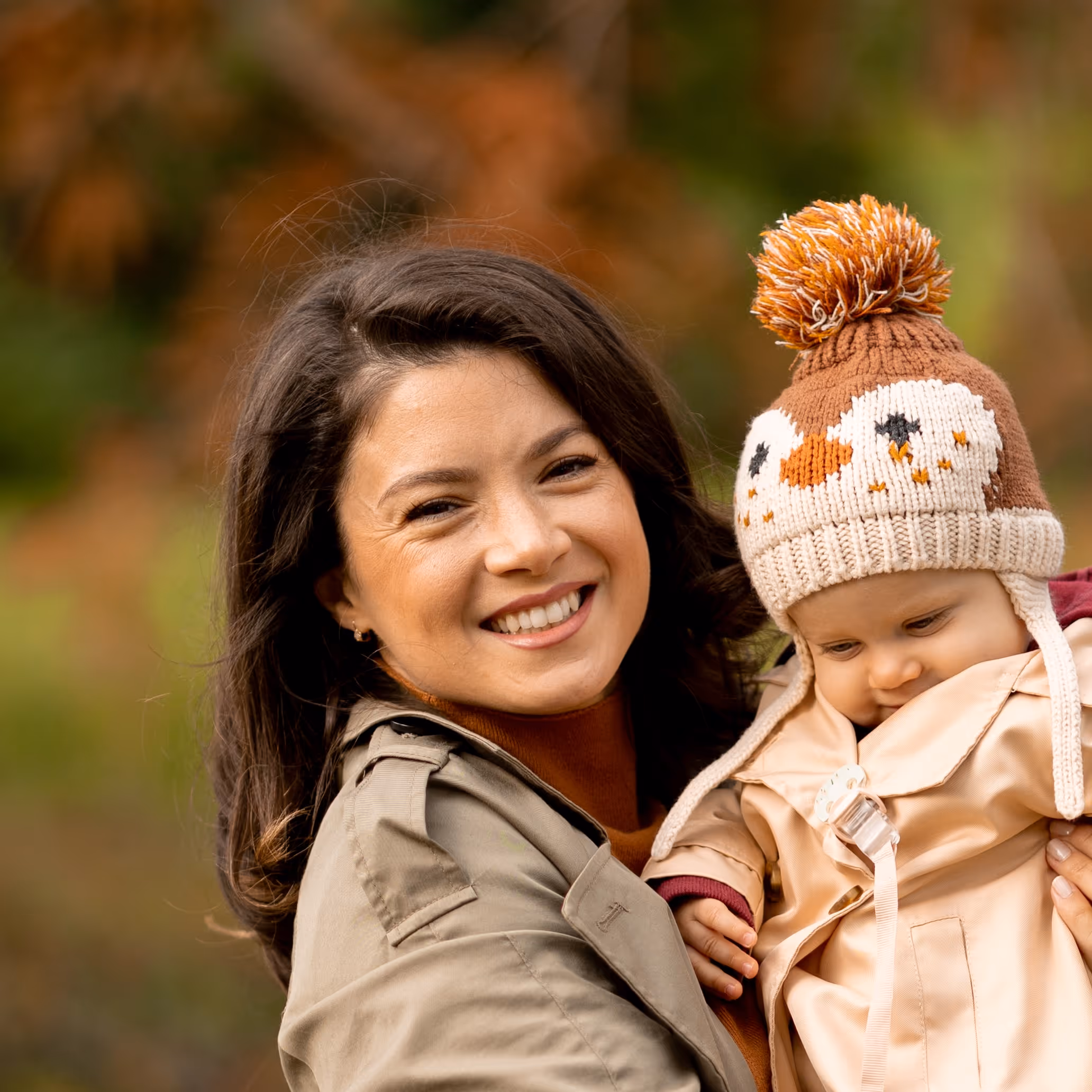 Smiling mother holding baby in autumn, wearing cute owl knit hat
