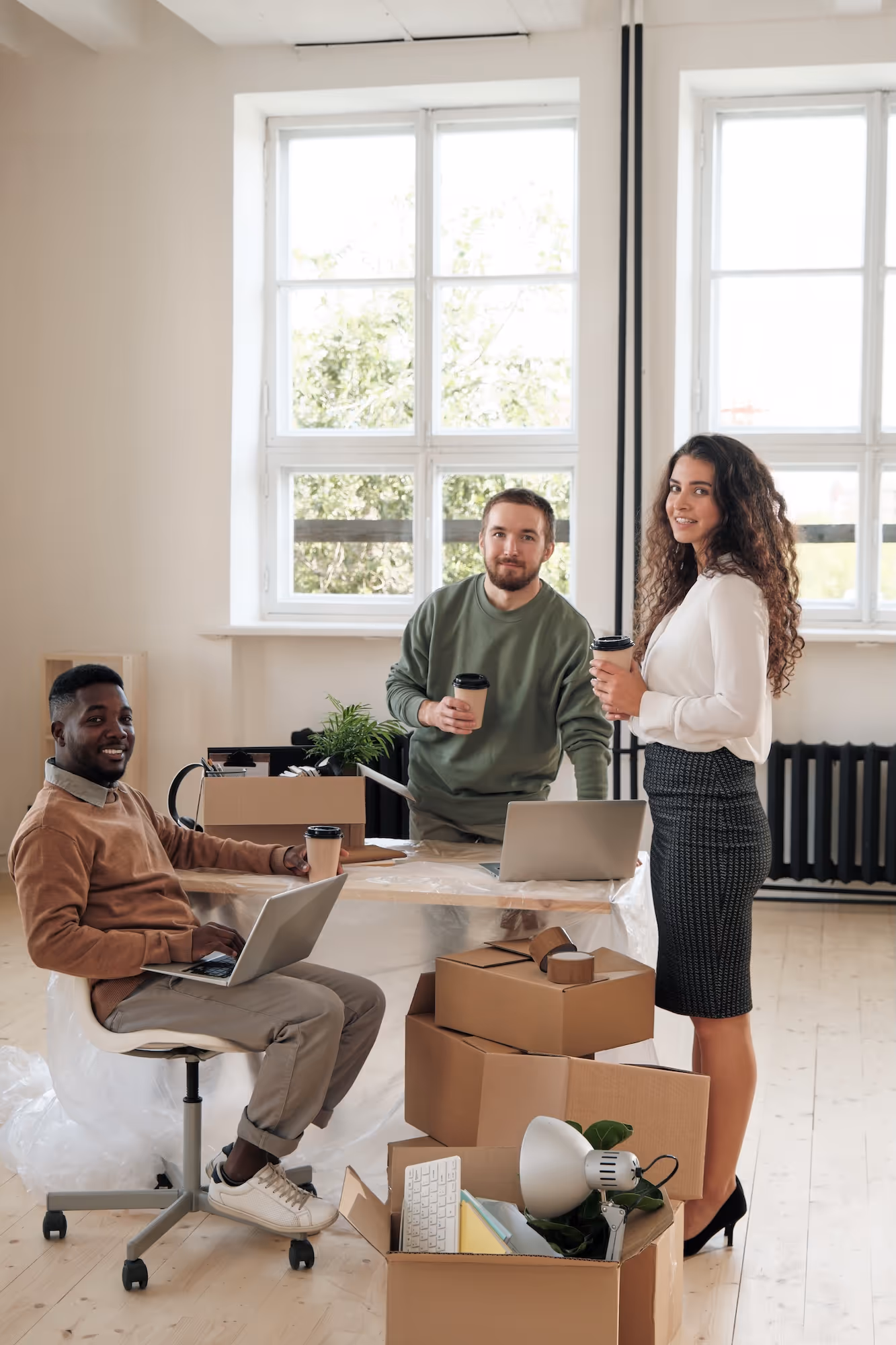 Three colleagues with coffee and moving boxes in a bright office space