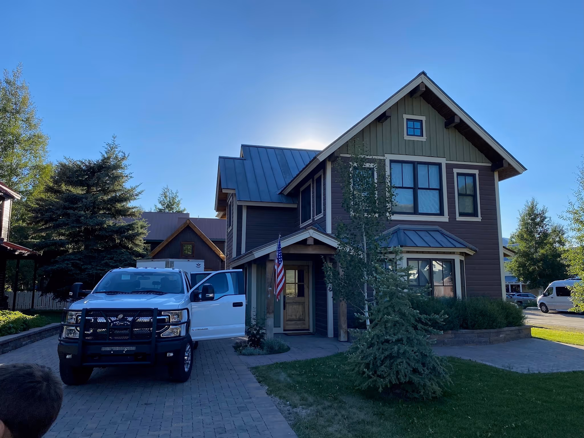 Two-story house with green siding and large windows, a white pickup truck parked on driveway.