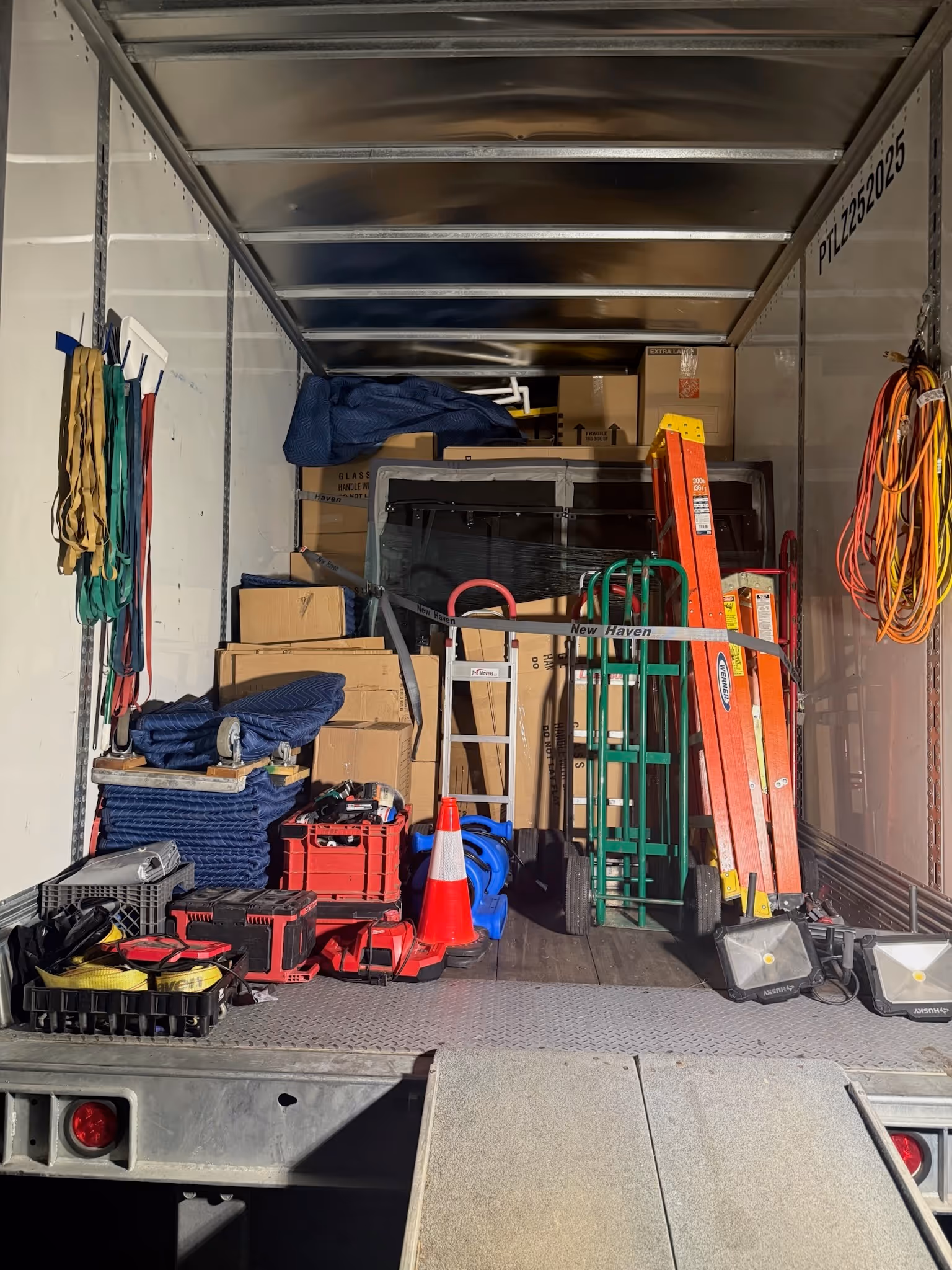 The inside of a moving truck loaded with supplies, including dollies, ladders, moving blankets, toolboxes, and coiled straps neatly hung along the walls.