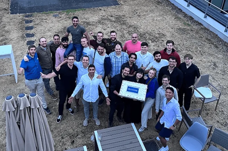 Group photo of the Shikenso team gathered outdoors, smiling and holding a celebratory cake during a company event.