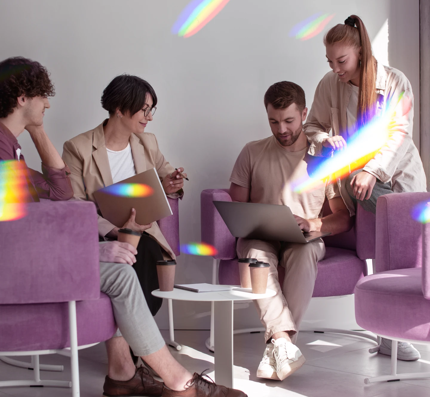 Group of four people collaborating with laptops in a bright modern office with colorful light reflections.