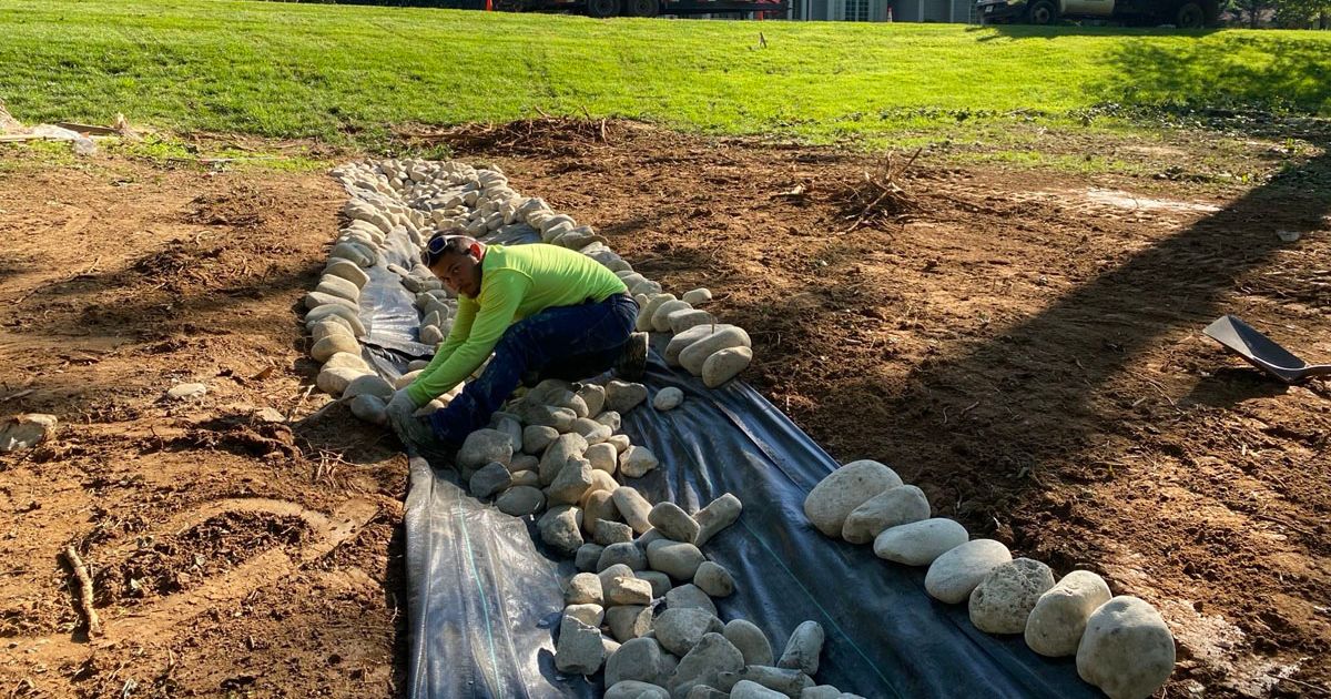 Worker installing drainage rocks on landscape fabric in outdoor area