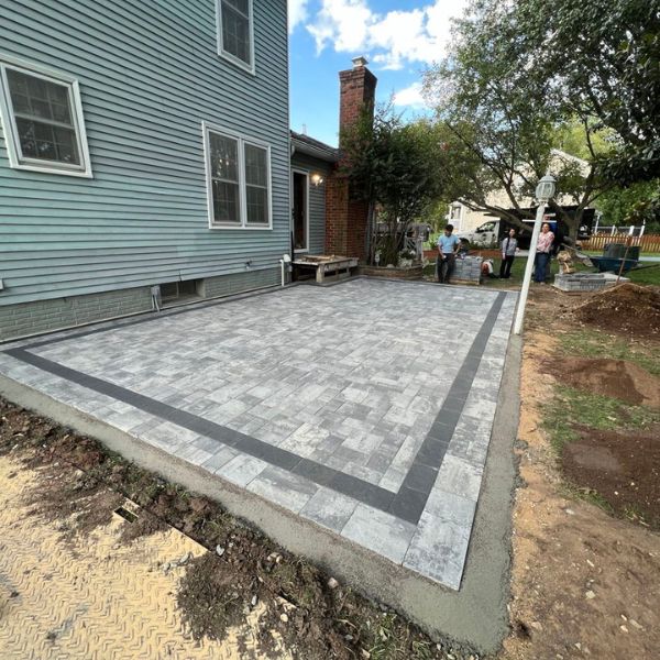 Newly installed gray paver patio with border, next to green siding house