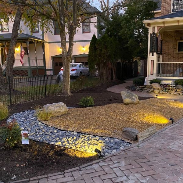 Nighttime landscaped front yard with stone path, rocks, and warm lighting