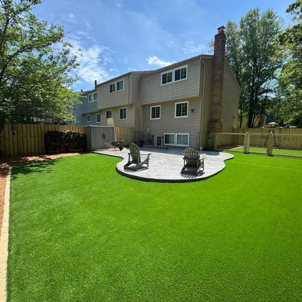 Green backyard with stone patio and two Adirondack chairs near suburban house