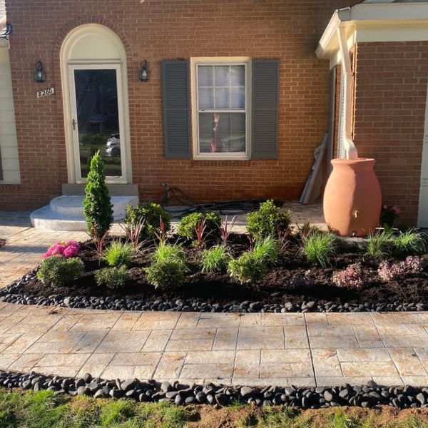 Landscaped front yard with brick house, plants, and stone border