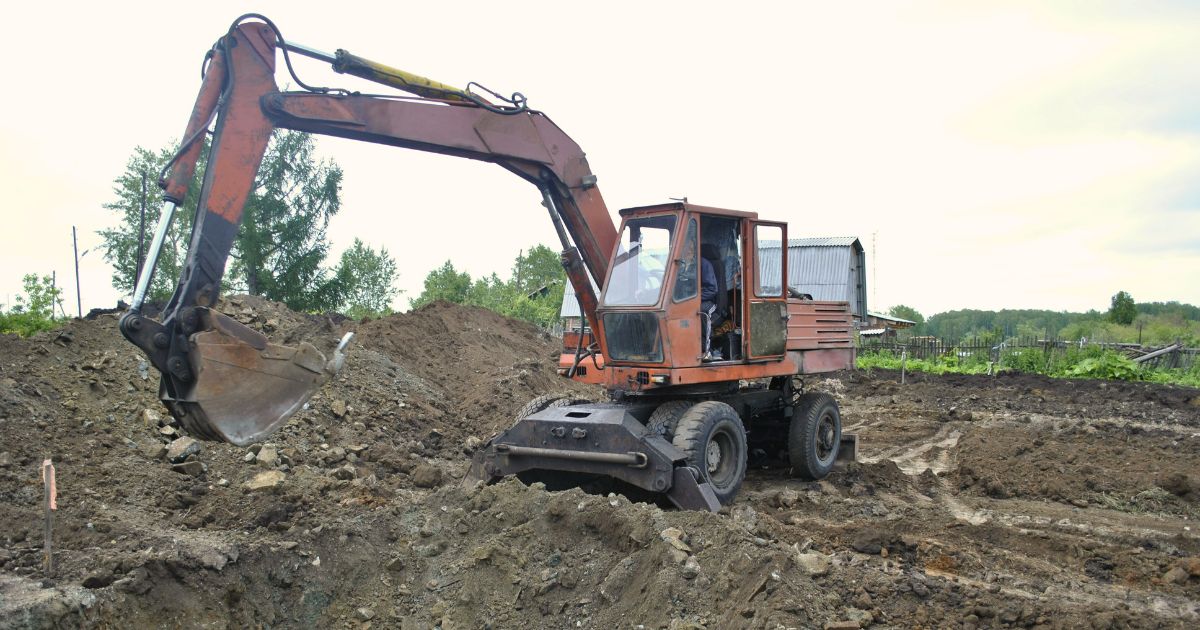 Orange excavator digging dirt at construction site with trees in background