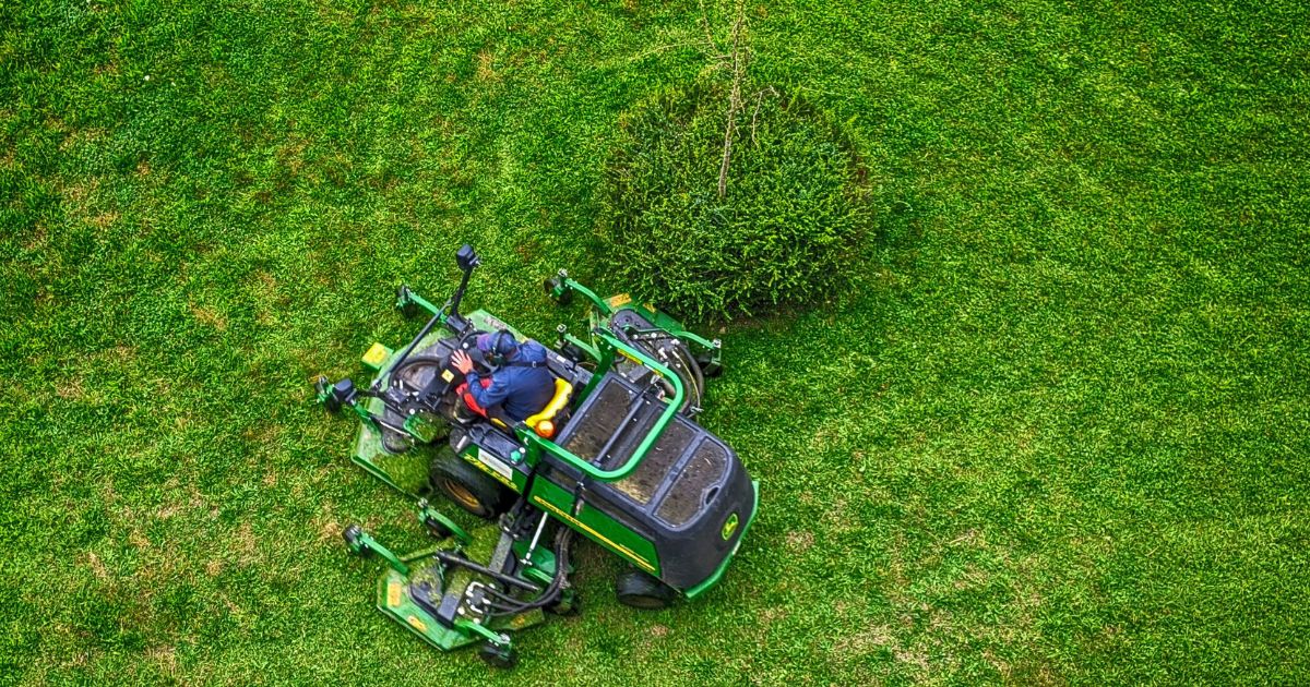 Large green commercial lawn mower cutting grass from aerial view
