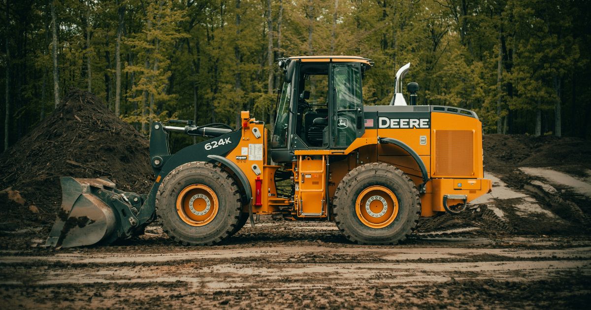 John Deere 624K wheel loader parked in muddy forest construction site