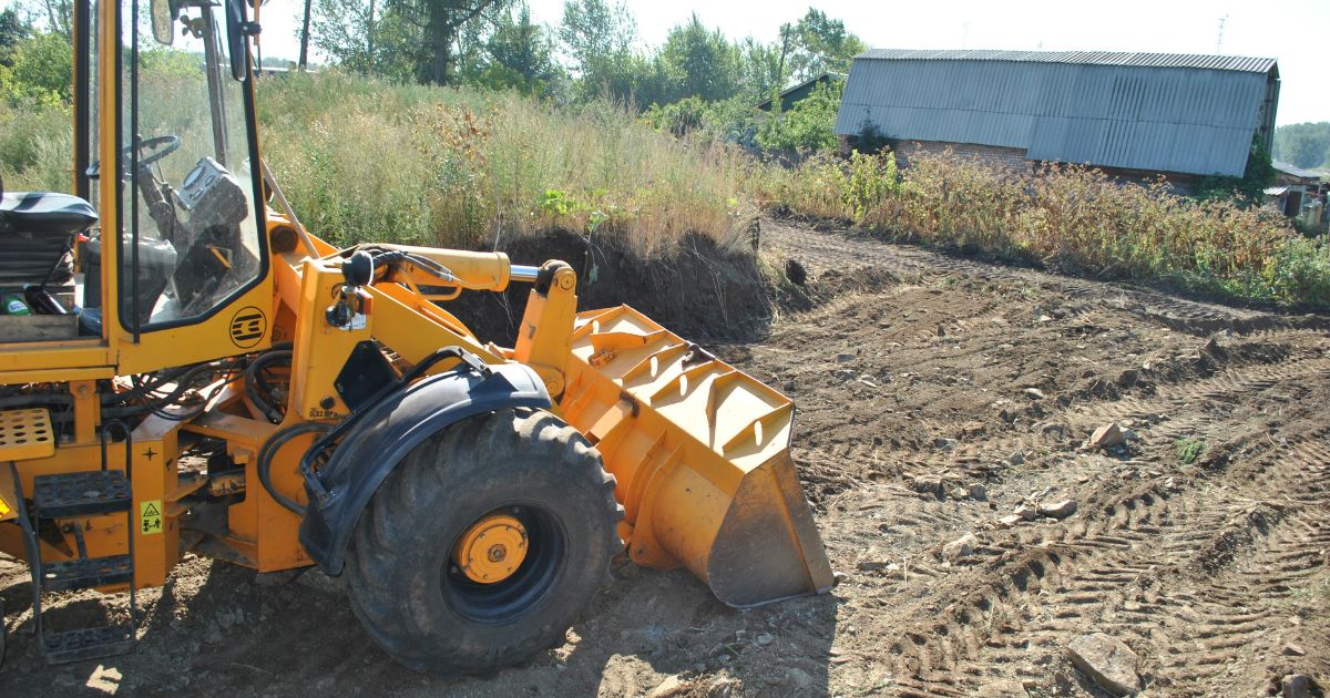 Yellow front-end loader working on dirt ground near rural barn