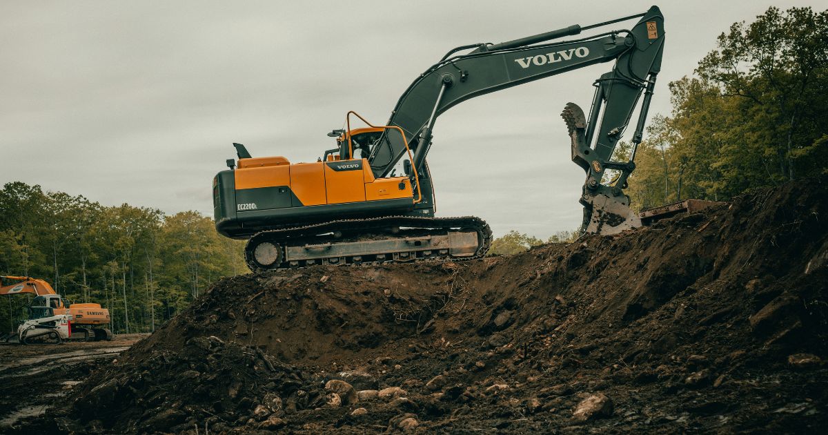 Yellow Volvo excavator digging on construction site with trees in background
