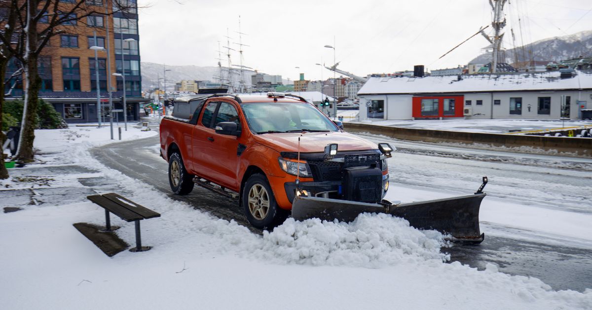 Orange pickup truck with snow plow clearing snowy urban street