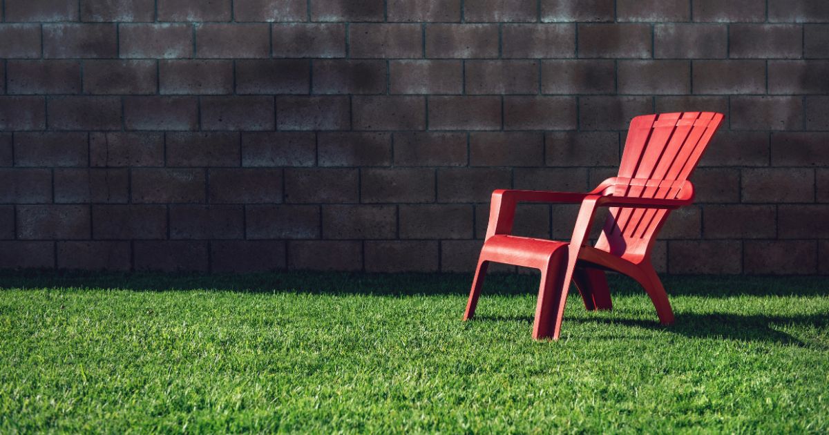 Bright red plastic chair sitting alone on green grass by brick wall