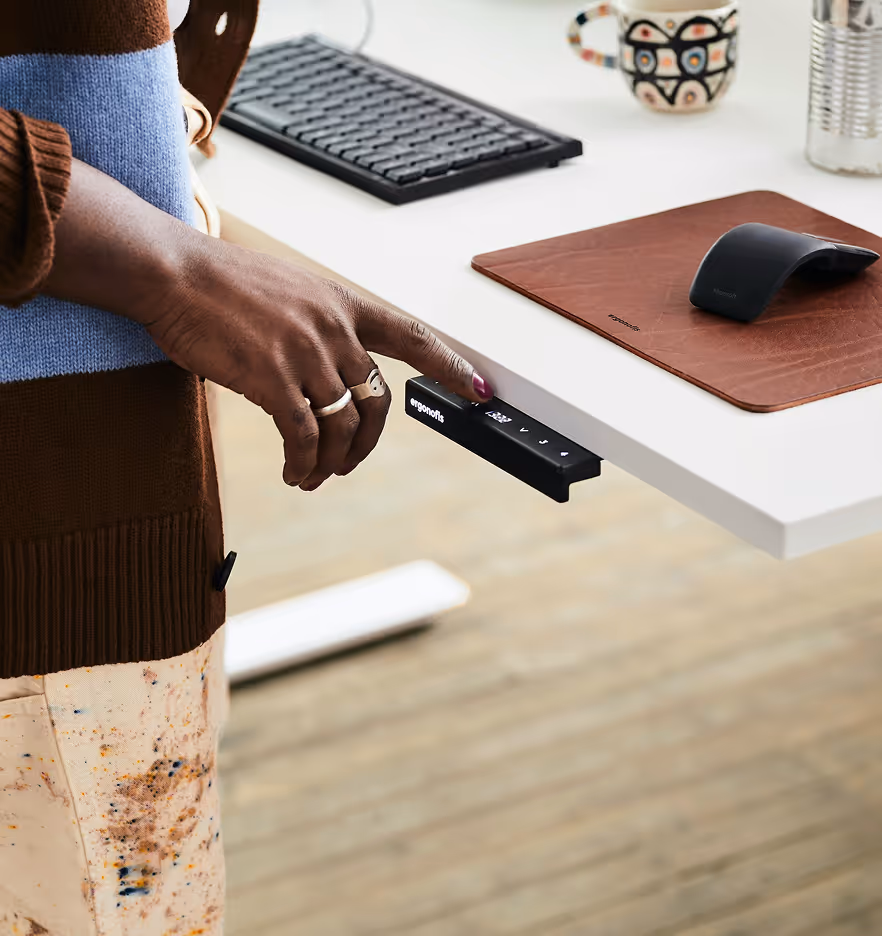 Hand justiert einen Bedienhebel an einem weißen Stehpult mit Tastatur, Maus und Tasse im Büro.