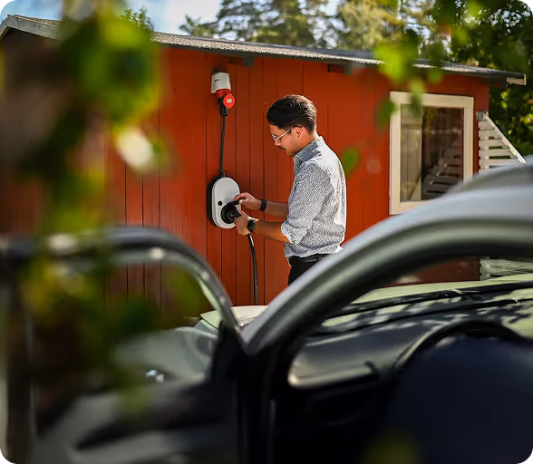 Mann lädt ein Elektroauto mit einer Wandladestation an einem roten Gebäude auf.