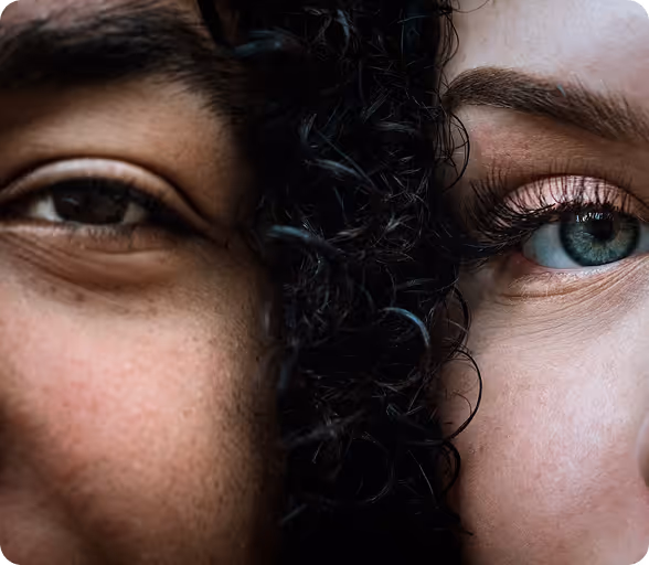 Nahaufnahme von zwei Gesichtshälften, eine mit dunkler Haut und braunem Auge, die andere mit heller Haut und blauem Auge, getrennt durch lockiges schwarzes Haar.