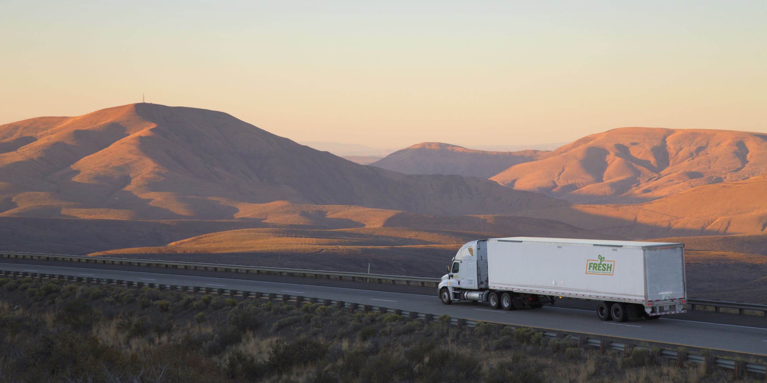 A Fresh Freight truck driving through rolling desert hills