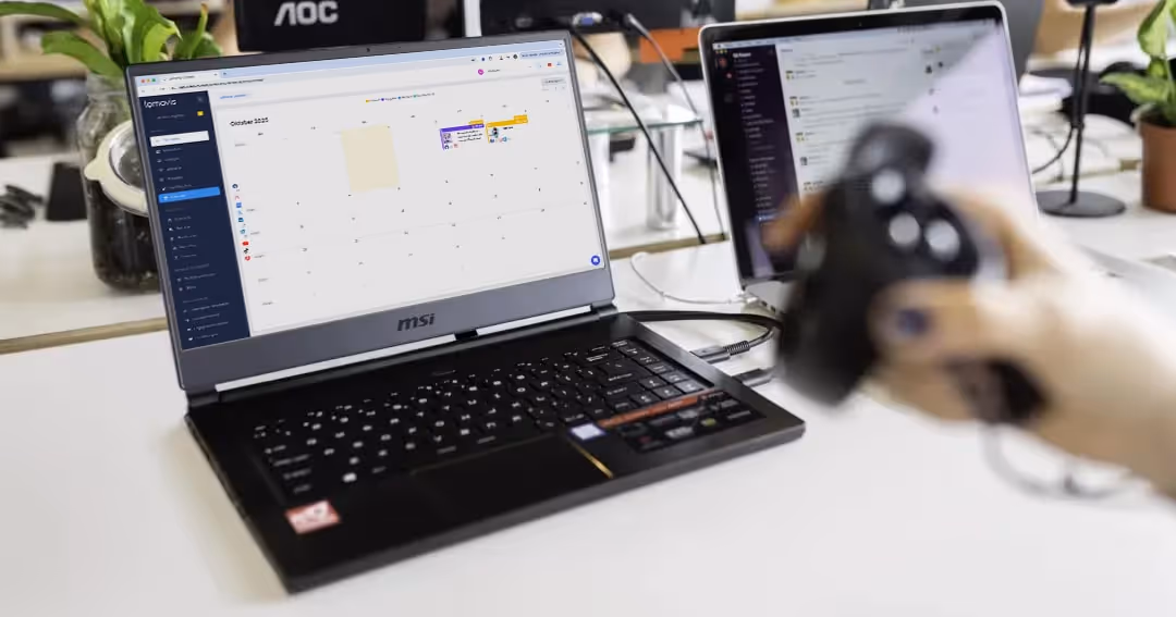 Ein MSI-Laptop auf einem Tisch zeigt einen digitalen Kalender für Oktober 2023; im Vordergrund hält eine Hand einen schwarzen Spiel-Controller.