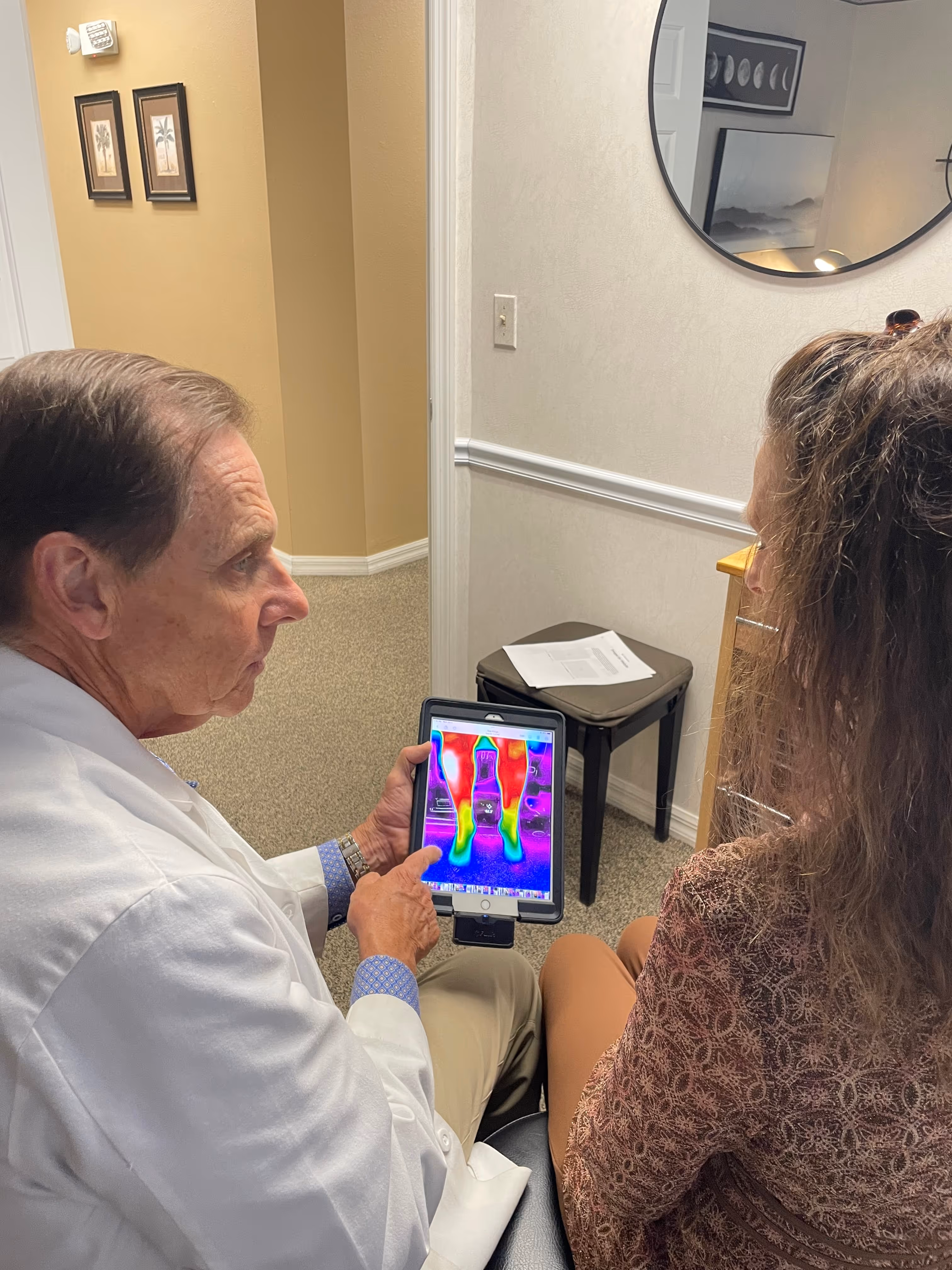 Dr. Carle sits with a patient and shows them on a screen an image of their neuropathy results via thermal scan.