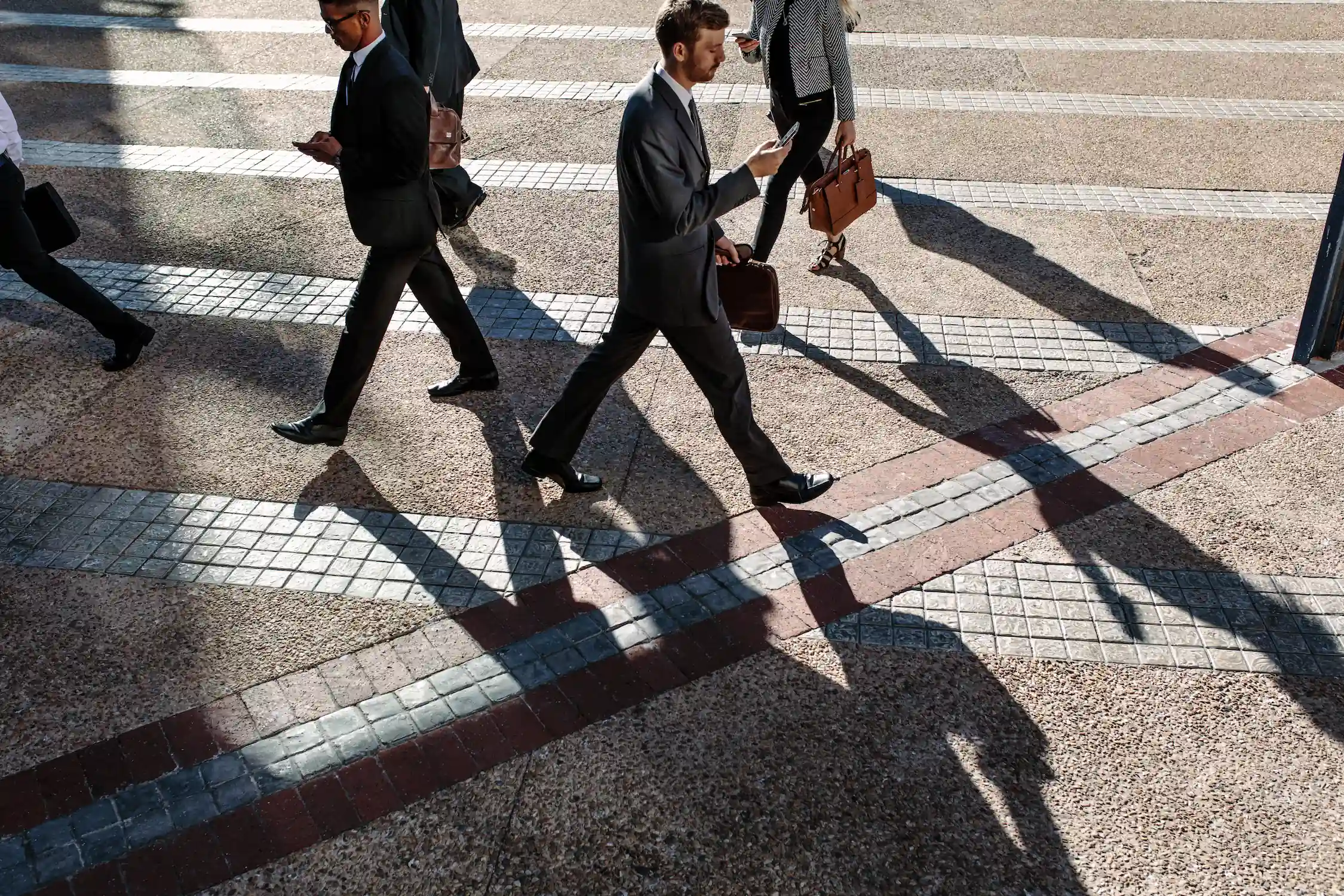 Business people holding their phones walking on a broad pathway.