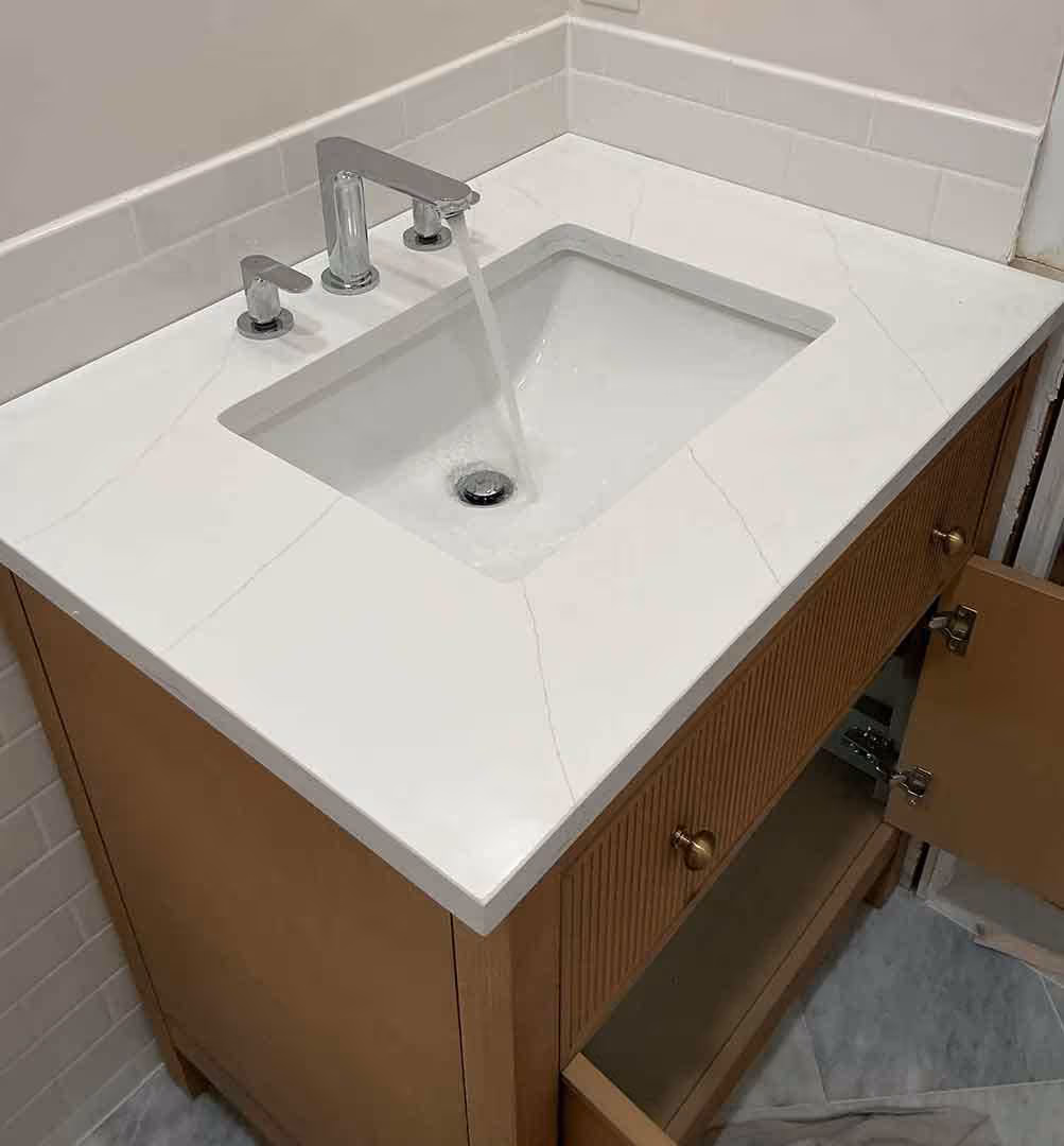 Modern bathroom sink and faucet installation with running water, showcasing clean plumbing work and high-quality craftsmanship on a quartz vanity countertop.