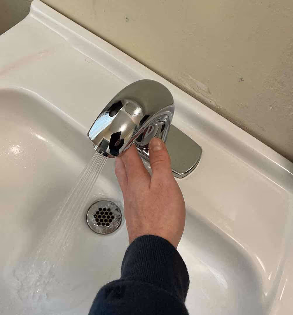 Close-up of chrome touchless faucet with running water, installed by Minuteman Plumbing for improved hygiene and water efficiency in bathroom sinks.