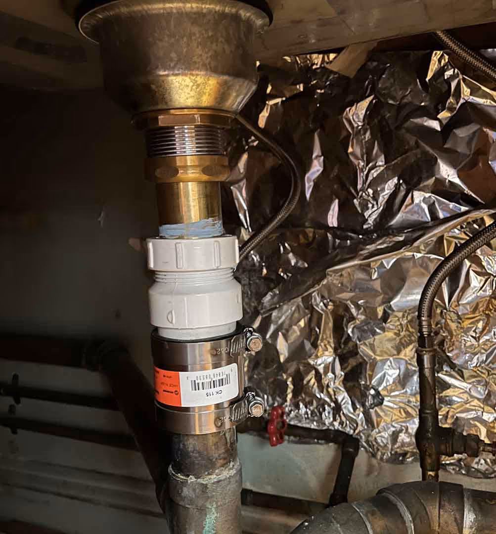 Close-up of a sink drain with a new coupling and fittings installed under the sink, showing professional plumbing repair and leak prevention work.