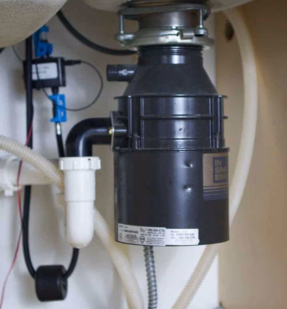 Under-sink garbage disposal unit professionally installed with secure plumbing and electrical connections by Minuteman Plumbing for kitchen waste management.