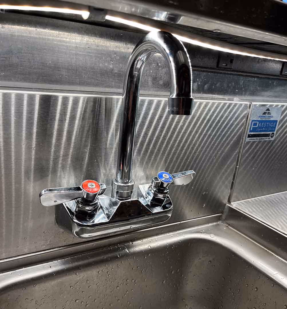 Commercial stainless-steel sink with dual-handle faucet installation by Minuteman Plumbing, Heating & Cooling, featuring separate hot and cold water controls for precision and durability.