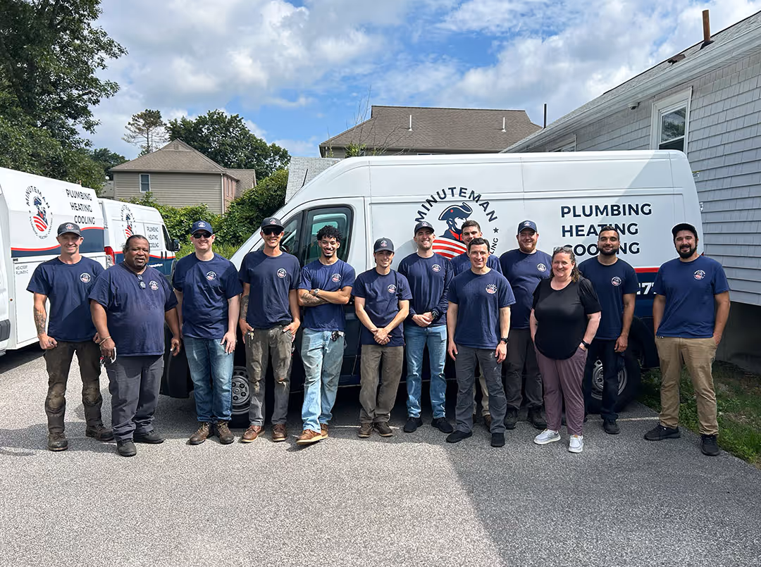 Team photo of Minuteman Plumbing, Heating & Cooling technicians and staff standing in front of company service vans in Massachusetts, showcasing their professional plumbing, heating, and cooling team.