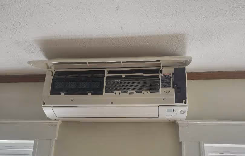 Wall-mounted ductless mini-split air conditioning unit with open cover showing interior filters during maintenance or inspection by Minuteman Plumbing, Heating & Cooling.