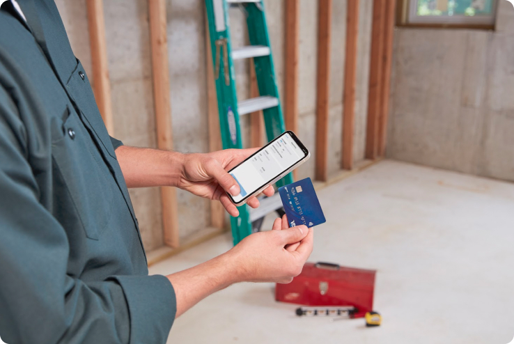 Small business owner in a customer's home, holding an iPhone and a credit card