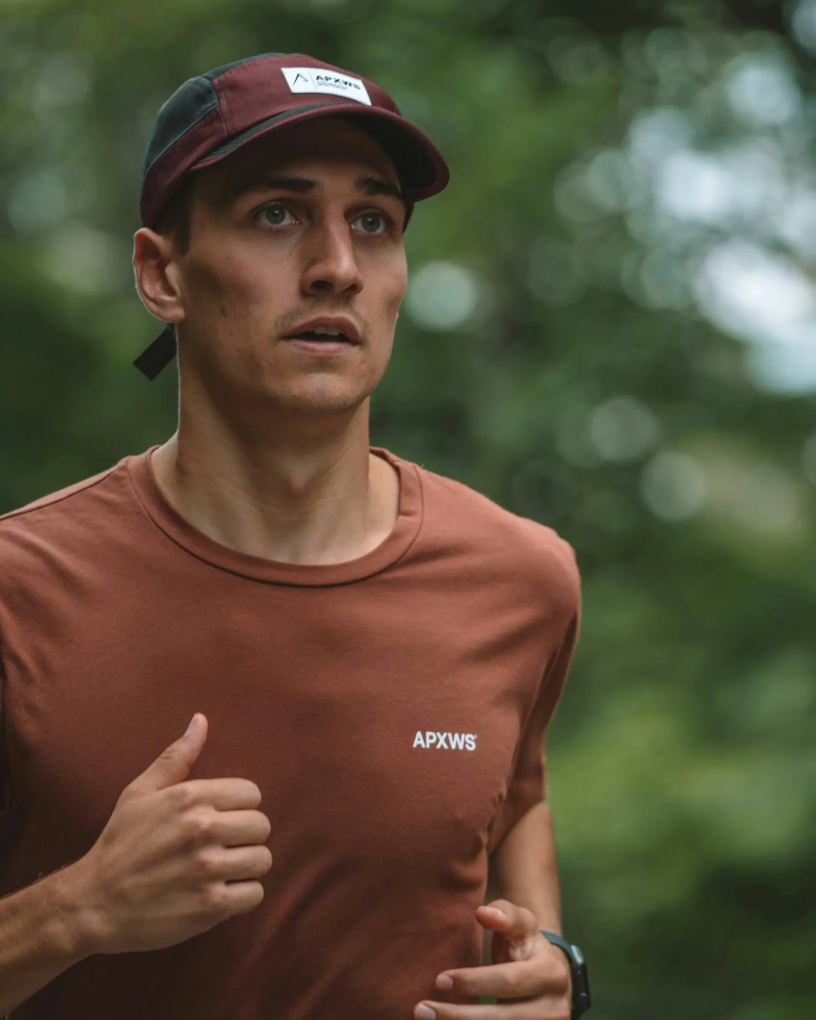 A young man running in a park with a cap.