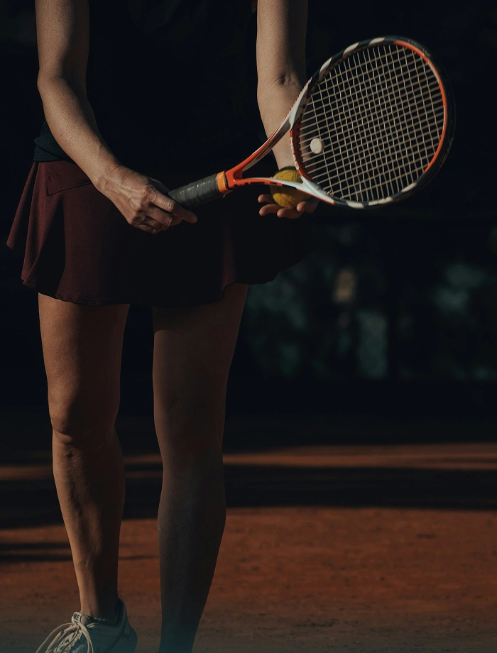 Woman holding tennis racket and ball, preparing to serve on a clay tennis court.