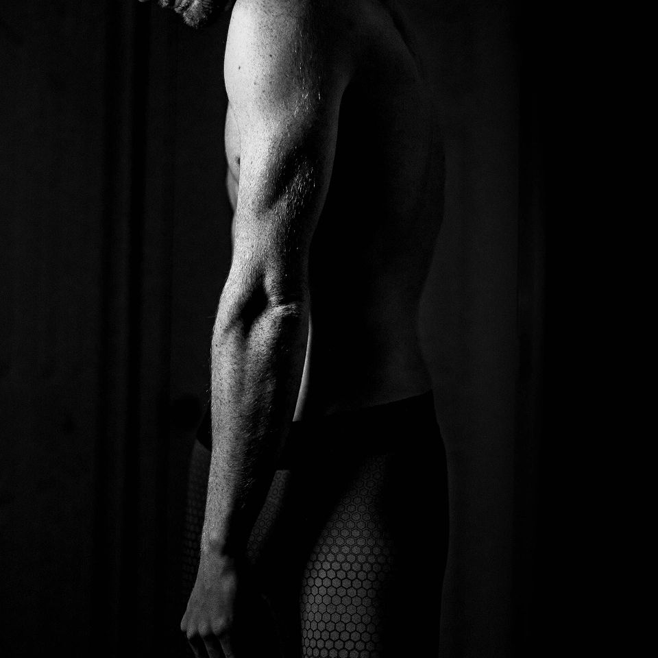 Black and white side view of a shirtless man wearing textured shorts, showing his arm and torso.