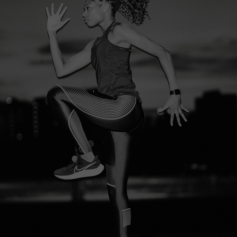 Athletic woman in running gear performing a high knee exercise outdoors at dusk.