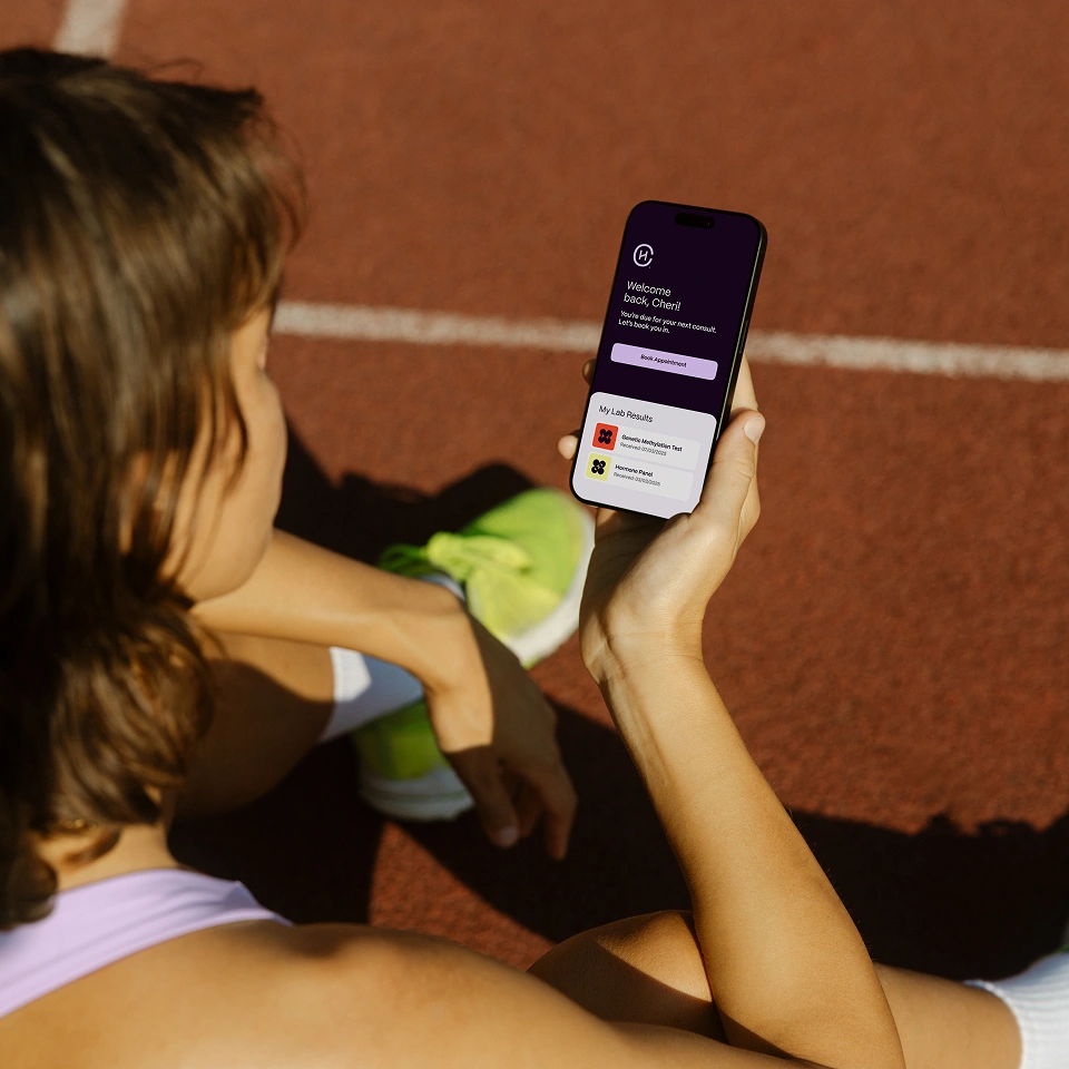 Person sitting on a running track holding a smartphone displaying a health app with lab results and appointment booking.