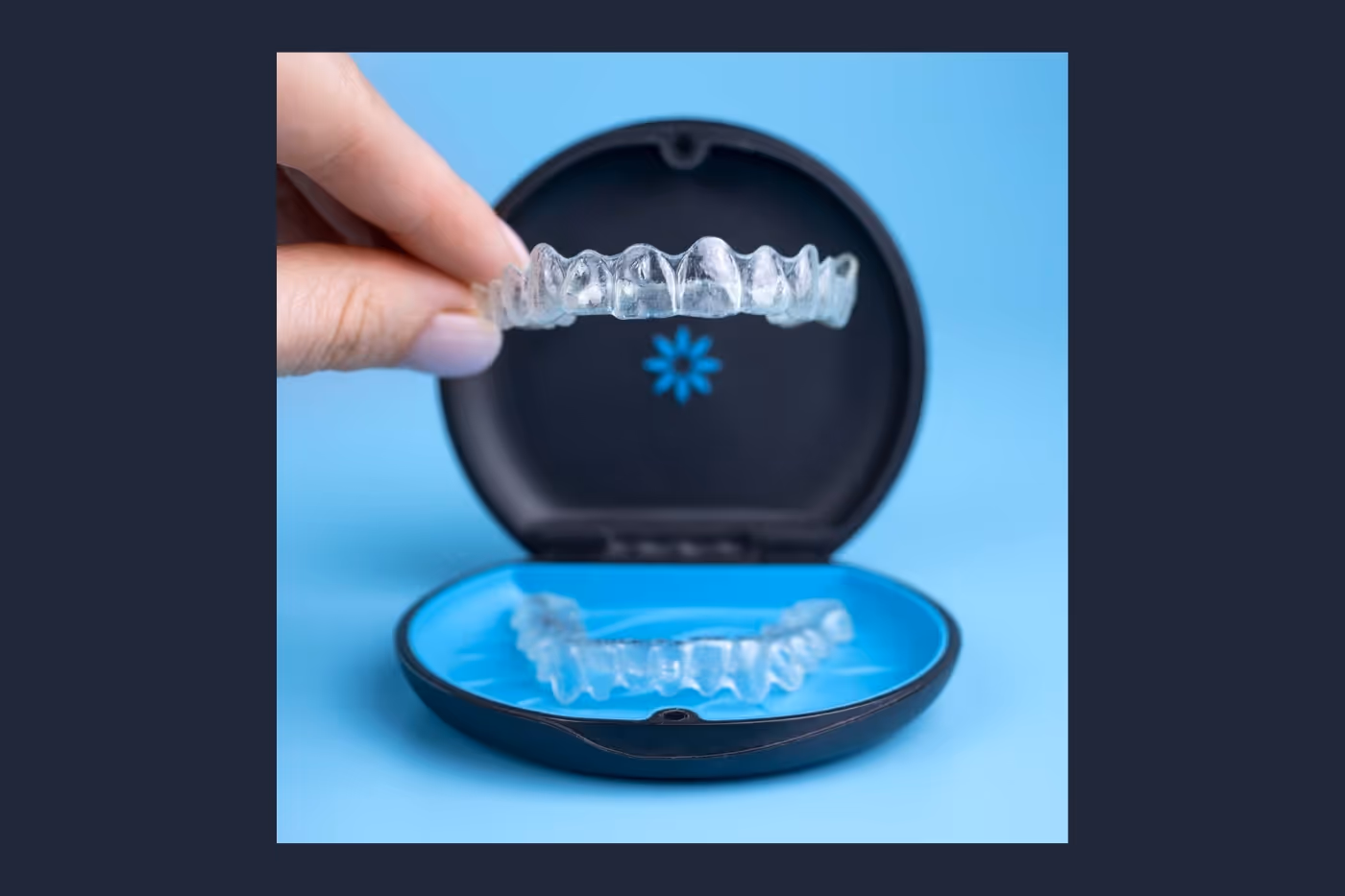 A close-up of a hand placing a clear Invisalign aligner into a black-and-blue storage case.