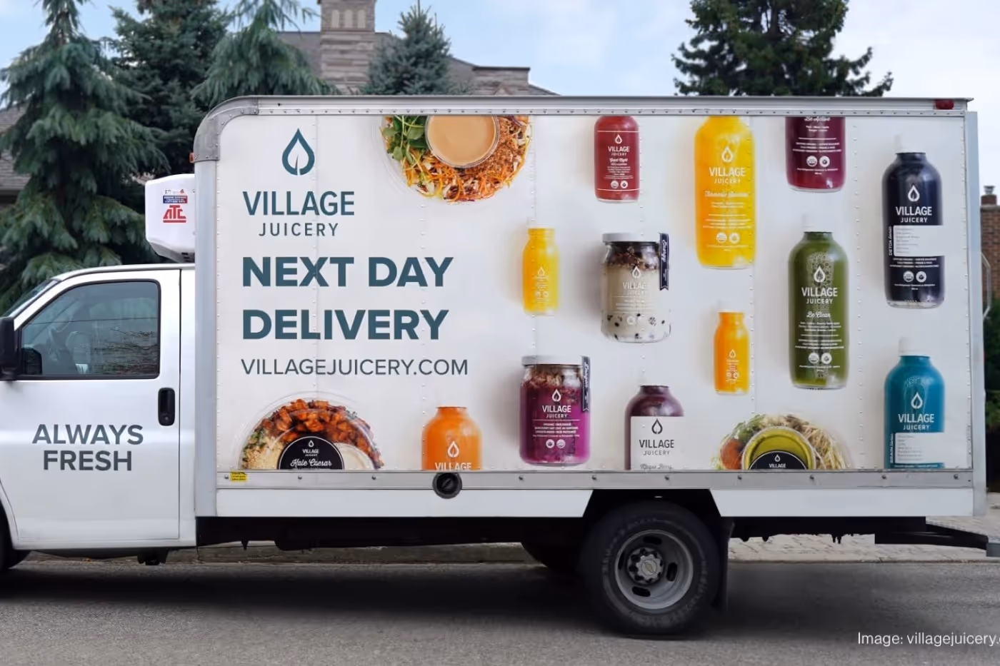 Village Juicery branded delivery truck with images of colorful juices and meals, promoting next-day delivery with the slogan "Always Fresh".