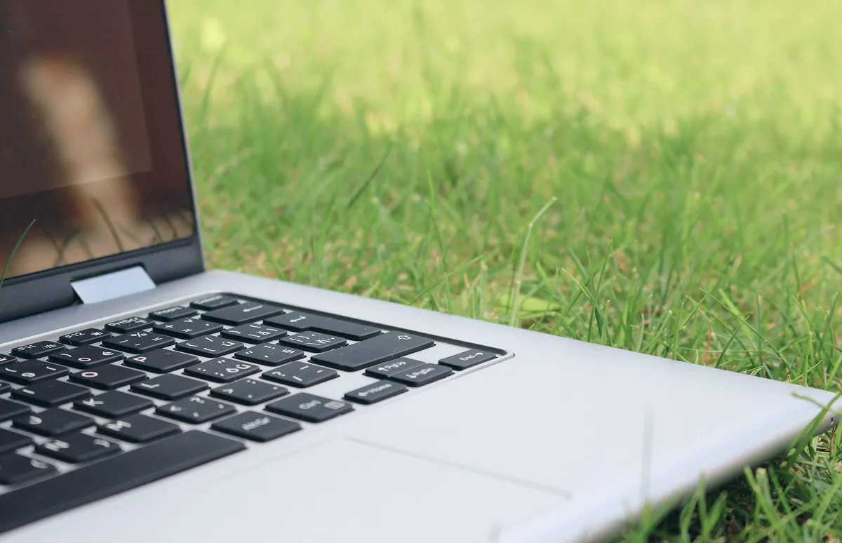 Close-up, side profile view of an open silver laptop sitting on a lush green lawn.