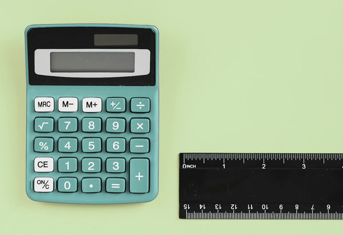 A teal calculator and a black ruler resting on a light green background.