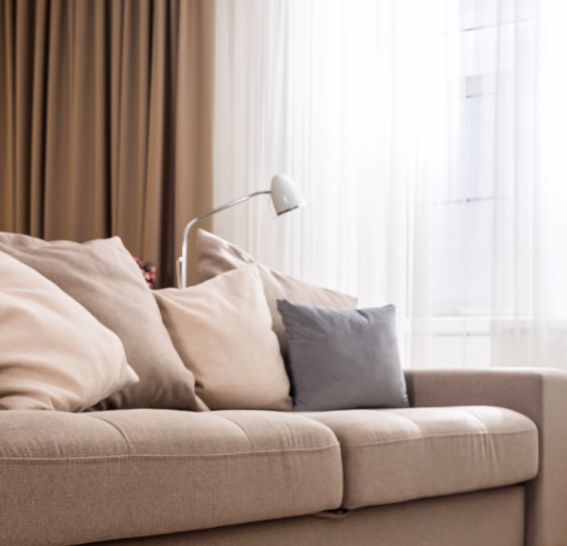 Beige fabric sofa with assorted cushions beside a large window and clean carpet.