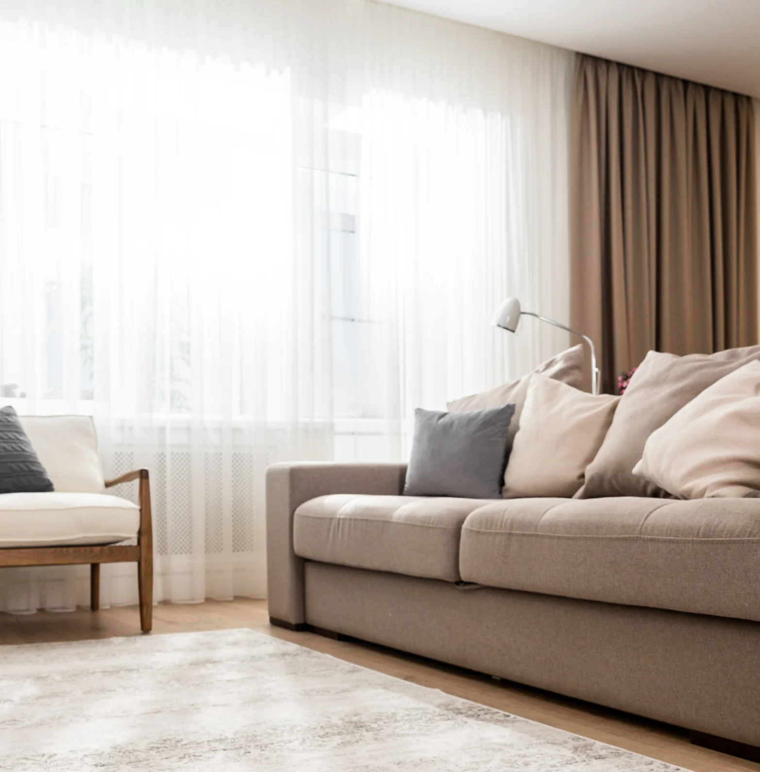 Bright living room with a beige fabric sofa, cushions, and a clean carpet by the window.