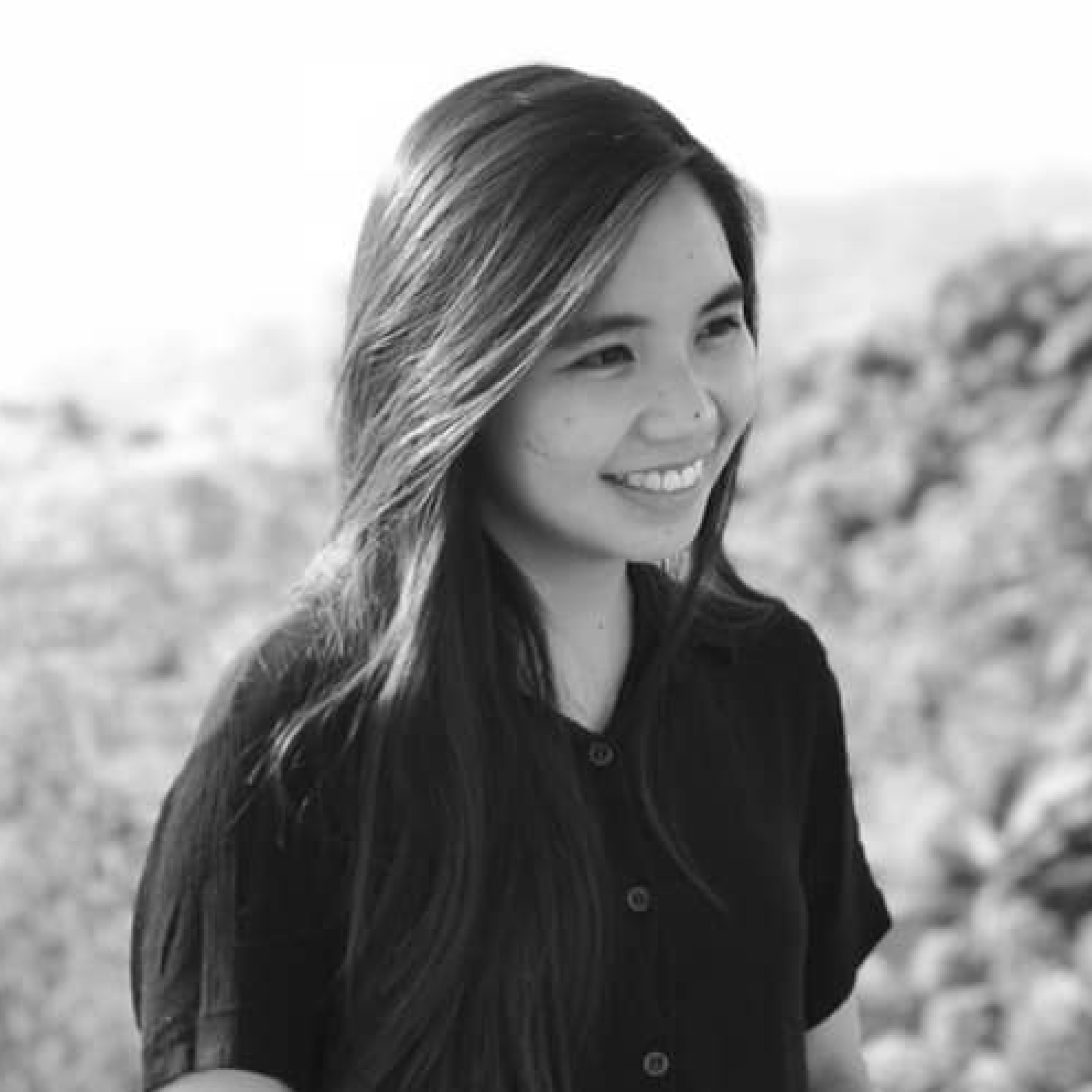 Smiling woman with shoulder-length brown hair wearing a black blazer and gold necklace against a dark background.